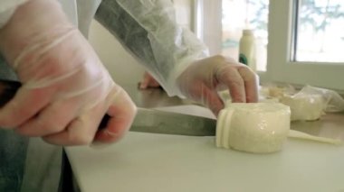 Beyaz önlüklü ve eldivenli bir kadın halloumi peyniri keser. Yakın çekim, yavaş çekim 4K. Çiftlikte peynir tatma. El yapımı, ev yapımı Yunan peyniri..