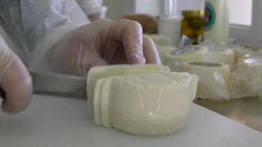 Beyaz önlüklü ve eldivenli bir kadın halloumi peyniri keser. Yakın çekim, yavaş çekim 4K. Çiftlikte peynir tatma. El yapımı, ev yapımı Yunan peyniri..
