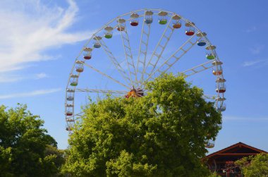 Bir yaz parkında mavi gökyüzüne karşı dönme dolap.