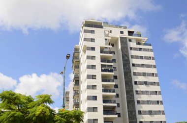 Modern yerleşim alanı. Yeni binanın yakınında çiçek açan ağaçlar. Lüks gayrimenkul. Bir daireye yatırım. Rahat balkonlar ve çiçek açan Royal Poinciana.