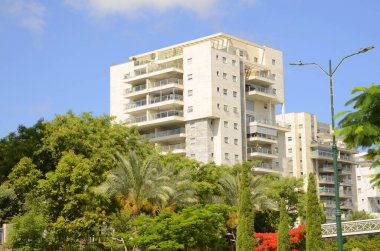 Modern yerleşim alanı. Yeni binanın yakınında çiçek açan ağaçlar. Lüks gayrimenkul. Bir daireye yatırım. Rahat balkonlar ve çiçek açan Royal Poinciana.