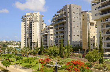 Modern yerleşim alanı. Yeni binanın yakınında çiçek açan ağaçlar. Lüks gayrimenkul. Bir daireye yatırım. Rahat balkonlar ve çiçek açan Royal Poinciana.