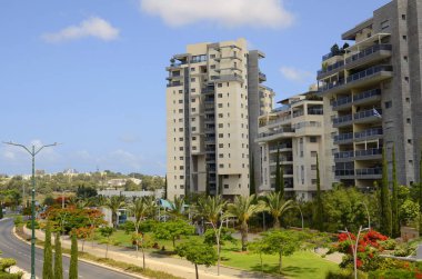 Modern yerleşim alanı. Yeni binanın yakınında çiçek açan ağaçlar. Lüks gayrimenkul. Bir daireye yatırım. Rahat balkonlar ve çiçek açan Royal Poinciana.