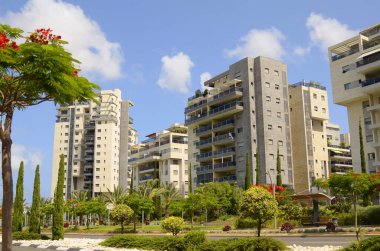 Modern yerleşim alanı. Yeni binanın yakınında çiçek açan ağaçlar. Lüks gayrimenkul. Bir daireye yatırım. Rahat balkonlar ve çiçek açan Royal Poinciana.