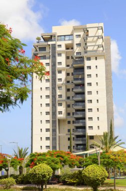 Modern yerleşim alanı. Yeni binanın yakınında çiçek açan ağaçlar. Lüks gayrimenkul. Bir daireye yatırım. Rahat balkonlar ve çiçek açan Royal Poinciana.