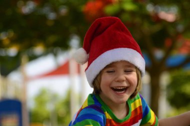 Noel Baba şapkalı ve güneş gözlüklü pozitif çocuk. Noel tatilleri. Aralık 'ta yaz