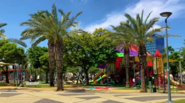 Güneşin altında güzel bir çocuk parkı, tropikal bir park, aileleriyle yürüyen çocuklar. İsrail Tel Aviv 2 Haziran 2024