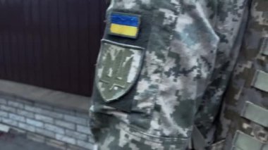 Ukraynalı asker yağmurda sokakta yürüyor. Askeri botlar, sırt çantası, Ukrayna bayrağı. Silahlı kuvvetler, vatanın savunucusu.