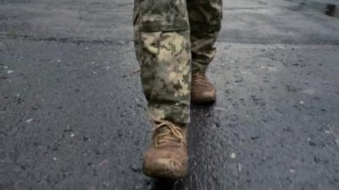 Ukraynalı asker yağmurda sokakta yürüyor. Askeri botlar, sırt çantası, Ukrayna bayrağı. Silahlı kuvvetler, vatanın savunucusu.