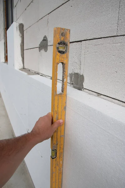 Construction worker insulating house wall with styrofoam insulatuion sheet, using of the construction spirit level.