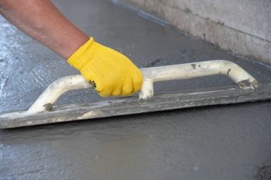 Mason evin önündeki kare malayla beton zemini düzleştiriyor ve tarıyor. İnşaat işi, kendin yap konsepti. Sarı eldivenli el..