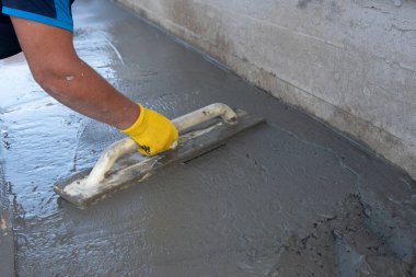 Mason evin önündeki kare malayla beton zemini düzleştiriyor ve tarıyor. İnşaat işi, kendin yap konsepti. Sarı eldivenli el..