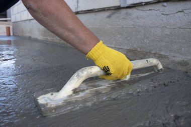 Mason evin önündeki kare malayla beton zemini düzleştiriyor ve tarıyor. İnşaat işi, kendin yap konsepti. Sarı eldivenli el..