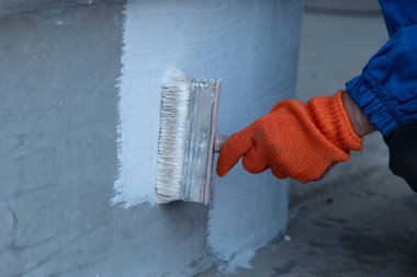 Beton duvarı beton polimer su geçirmez zarı ile kapatın. Beyaz bir fırçayla su geçirmez. Su geçirmez kaplama beyaz..