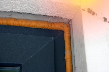 Tamamlanmamış, ısı yalıtımlı maddeyle dolu teknolojik dikişli bir evin parçası. Poliüretan köpükle açılan pencerenin izolasyonu. Kapat.