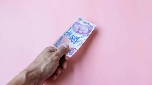 Hands holding 200 Lira banknote on pink background, Background Lira banknotes, Two hundred Lira on pink backgrond, Pile of banknotes on pink background with copy space.