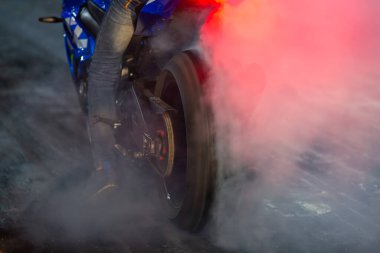 Motosiklet lastik yakıyor, motosiklet tekerleği sürükleniyor, beyaz sigara içiyor, motosiklet tekerleği yarış pistinde beyaz dumanlı.