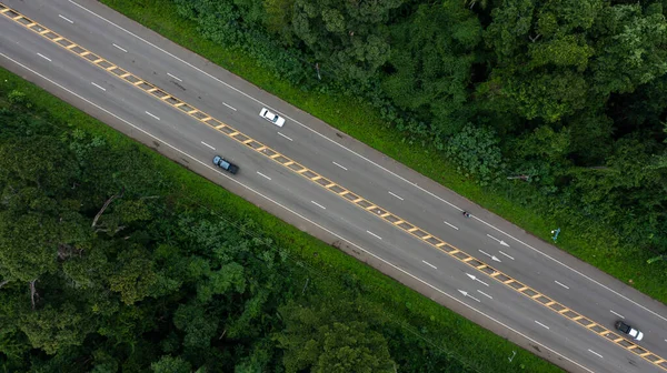 Aerial top view countryside highway asphalt road with forest, Aerial view road through the forest, Traffic highway between the natural parkland, Asphalt road through green tropical rainforest nature landscape.