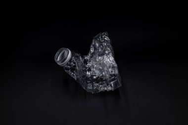 Siyah zemin üzerinde ezilmiş plastik su şişesi, çevreyi kurtarmak, siyah zemin üzerinde bükülmüş plastik su şişesi..