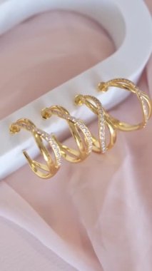 Beyaz kürsüde katlanmış pembe bezin üzerinde duran Hoop küpeleri. Dikey video.