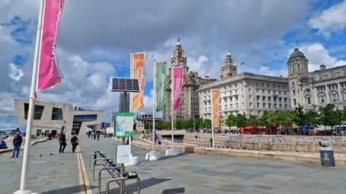 İnsanlar Liverpool rıhtımındaki Liverpool rıhtımında geziniyor ve The Three Graces ve diğer binalarda.