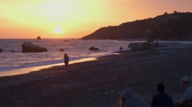 İnsanlar Petra tou Romiou 'da, Kıbrıs' ın Paphos kentinde, Afrodit 'in Yunan mitolojisinde doğduğu yerde gün batımının keyfini çıkarıyorlar..
