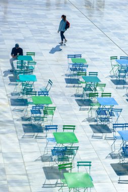 Atina, Yunanistan - 27 Ekim 2024: Stavris Niarchos Vakfı 'nın dışındaki bir kafede bir erkek, bir kadın ve geometrik desenli renkli metal masa ve sandalyelerin soyut sahnesi.