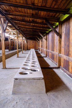 Auschwitz-Birkenau 'daki tuvalet binası. Birden fazla deliği olan beton bir yapı. Mahkumların maruz kaldığı sağlıksız ve insanlık dışı koşulları gösteriyor..