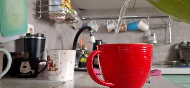 Mutfak masasında yeşil çay olan kırmızı seramik bardak.