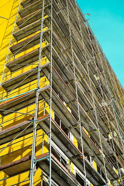 Red scaffolding near a yellow high-rise building. Construction of a multi-storey.