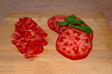 Ahşap zemin üzerinde fesleğen olan dilimlenmiş kırmızı taze domates.