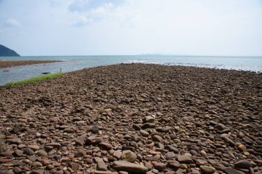 Tayland 'da gün ışığında kumsalda kayalar ve taşlar. Sahilin arka planında çakıl taşlarıyla deniz manzarası..