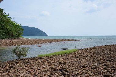 Tayland 'da gün ışığında kumsalda kayalar ve taşlar. Sahilin arka planında çakıl taşlarıyla deniz manzarası..