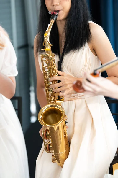 Young woman saxophonist with an instrument stands by the window. Cozy home interior. Concept of hobbies, inner world, development of talents, music school.