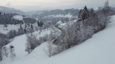 Romanya 'daki dağların ortasından geçen rüzgarlı ve eğimli bir yolun 4K' lık kış görüntüsü