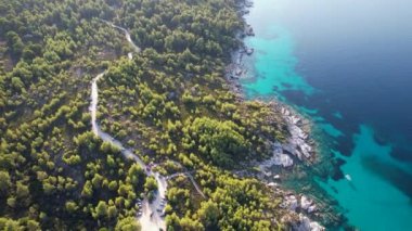 Yunanistan 'ın Sithonia kentindeki sembolik turkuaz ve safir Cennet plajlarının Atos Dağı manzaralı insansız hava aracı videosu. Yüksek kayalıklarla çevrili güzel bir kumsal manzarası.