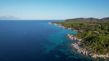 Yunanistan 'ın Sithonia kentindeki sembolik turkuaz ve safir Cennet plajlarının Atos Dağı manzaralı insansız hava aracı videosu. Yüksek kayalıklarla çevrili güzel bir kumsal manzarası.
