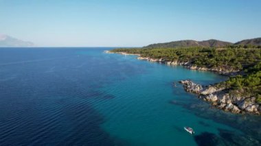 Yunanistan 'ın Sithonia kentindeki sembolik turkuaz ve safir Cennet plajlarının Atos Dağı manzaralı insansız hava aracı videosu. Yüksek kayalıklarla çevrili güzel bir kumsal manzarası.