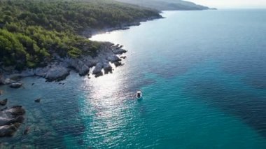 Yunanistan 'ın Sithonia kentindeki sembolik turkuaz ve safir Cennet plajlarının Atos Dağı manzaralı insansız hava aracı videosu. Yüksek kayalıklarla çevrili güzel bir kumsal manzarası.
