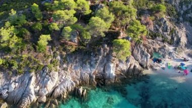 Yunanistan 'ın Sithonia kentindeki sembolik turkuaz ve safir Cennet plajlarının Atos Dağı manzaralı insansız hava aracı videosu. Yüksek kayalıklarla çevrili güzel bir kumsal manzarası.