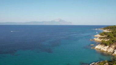 Yunanistan 'ın Sithonia kentindeki sembolik turkuaz ve safir Cennet plajlarının Atos Dağı manzaralı insansız hava aracı videosu. Yüksek kayalıklarla çevrili güzel bir kumsal manzarası.
