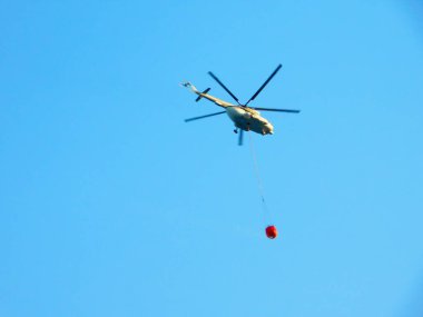 Yangın söndürme helikopteri sabah erken saatlerde orman yangınını söndürmek için yorulmadan su kovası taşır.