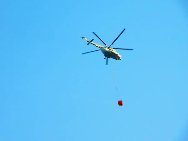 Fire fighting helicopter tirelessly carry water bucket to extinguish the forest fire from early morning