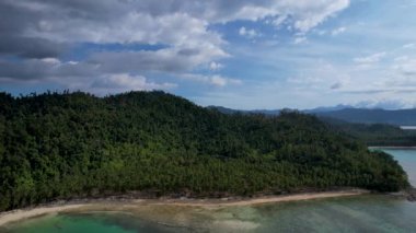 Güneşli bir günde, arkasında bulutlar olan büyülü palmiye ağaçları ve kristal mavi sularla güzel Coconut plajının 4K Hava Aracı videosu. Port Barton, Palawan Filipinleri