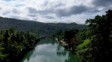 4K Zümrüt Loboc nehrinin nehir kenarındaki yolu ve Bohol, Filipinler 'deki evleri gösteren İHA videosu.