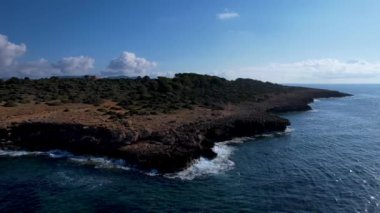 4K Hava Aracı 'nın Mallorca' da kristal berrak suyla çekilmiş videosu güneşli bir yaz gününde sert dalgalar kayalıklara çarpıyor.