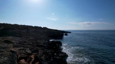 4K Hava Aracı 'nın Mallorca' da kristal berrak suyla çekilmiş videosu güneşli bir yaz gününde sert dalgalar kayalıklara çarpıyor.