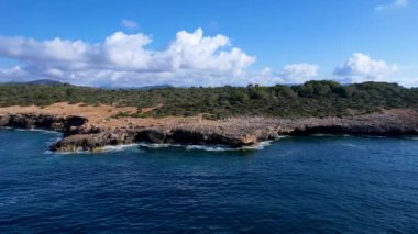 4K Hava Aracı 'nın Mallorca' da kristal berrak suyla çekilmiş videosu güneşli bir yaz gününde sert dalgalar kayalıklara çarpıyor.