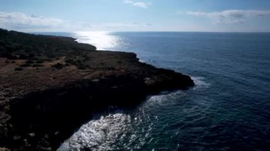 4K Hava Aracı 'nın Mallorca' da kristal berrak suyla çekilmiş videosu güneşli bir yaz gününde sert dalgalar kayalıklara çarpıyor.