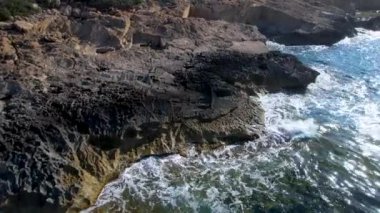 4K Hava Aracı 'nın Mallorca' da kristal berrak suyla çekilmiş videosu güneşli bir yaz gününde sert dalgalar kayalıklara çarpıyor.